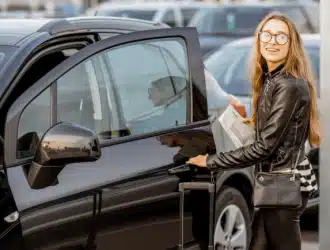 mulher loira com óculos abrindo a porta de um carro preto enquanto segura uma mala