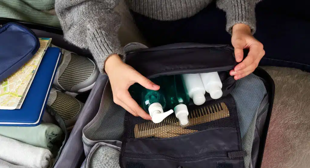 Uma garota coloca cosméticos em uma mala com roupas e acessórios para a viagem.