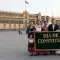 imagem de várias pessoas na frente do palácio do méxico com uma bandeira escrita Dia de la Constitución