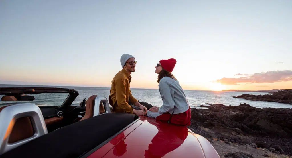 casal em um pôr do sol na praia sentado em um carro
