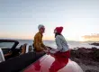 casal em um pôr do sol na praia sentado em um carro