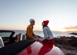 casal em um pôr do sol na praia sentado em um carro