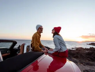 casal em um pôr do sol na praia sentado em um carro