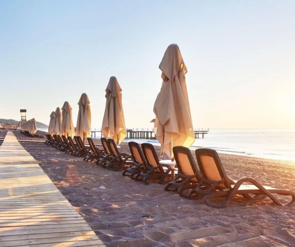 céu azul e sol em uma praia na Europa, areia e várias cadeiras com guarda-sol