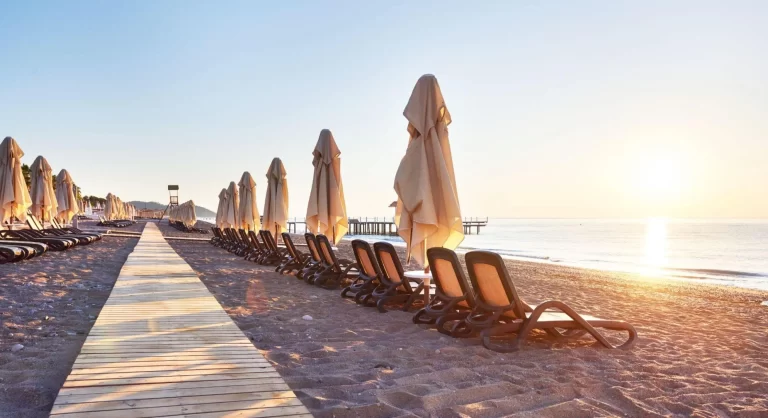 céu azul e sol em uma praia na Europa, areia e várias cadeiras com guarda-sol