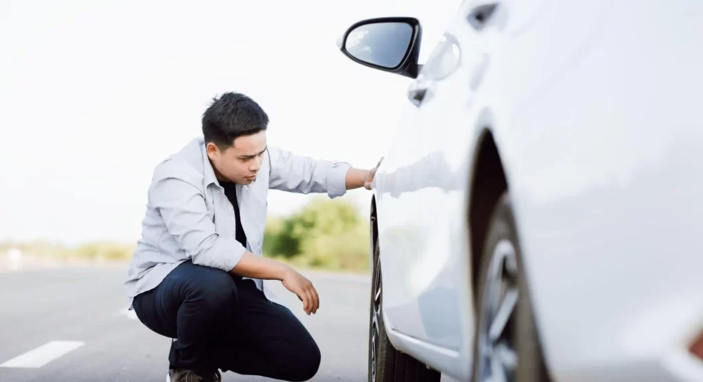 homem de camiseta branca abaixado olhando pneu de um carro branco