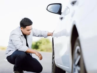 homem de camiseta branca abaixado olhando pneu de um carro branco