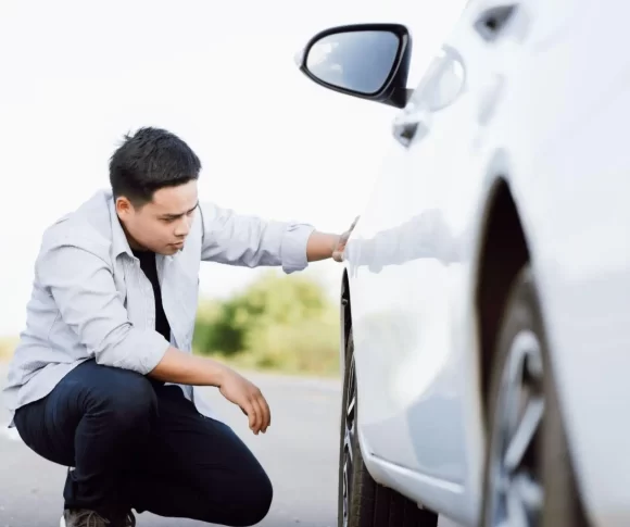 homem de camiseta branca abaixado olhando pneu de um carro branco