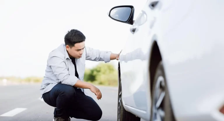 homem de camiseta branca abaixado olhando pneu de um carro branco