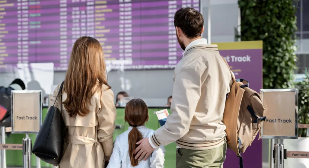 Familia esperando en el aeropuerto frente a la pantalla de salidas y llegadas tras un retraso de vuelo