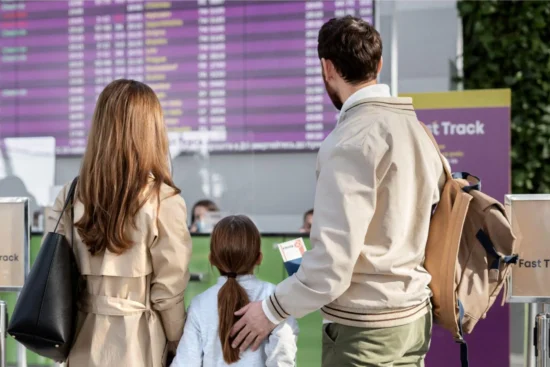 Familia esperando en el aeropuerto frente a la pantalla de salidas y llegadas tras un retraso de vuelo