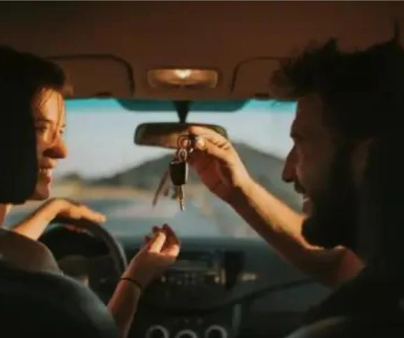 mulher e homem dentro do carro sorrindo com homem passando a chave para ela