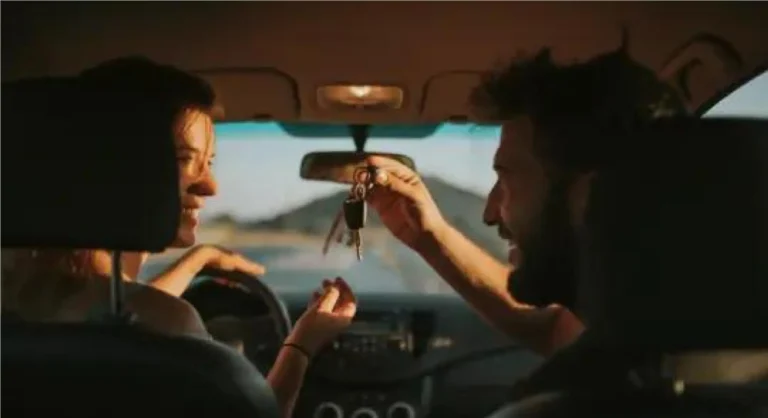 mulher e homem dentro do carro sorrindo com homem passando a chave para ela