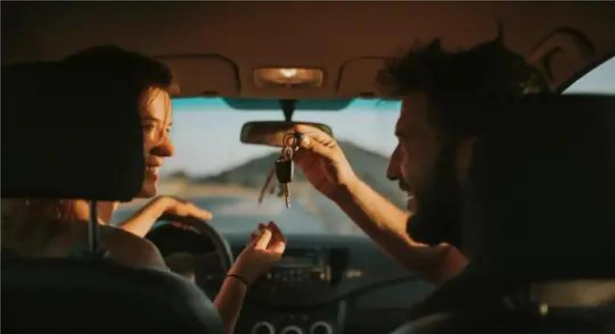 mulher e homem dentro do carro sorrindo com homem passando a chave para ela