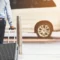 Homem com camisa azul e calça escura caminhando com mala de viagem grande e maleta de mão em um estacionamento, ao lado de um carro ao fundo, ambiente de transporte e viagem