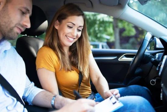 Aquí tienes la traducción directa de la frase aplicando la conjugación de tú (asumiendo el papel protagónico en la acción): "Una pareja en el interior de un carro en movimiento, contigo sonriendo mientras ajustas o sujetas el tablero, y el hombre a tu lado, ambos usando cinturones de seguridad y manejando con atención al tránsito