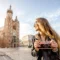Mulher ao ar livre em um passeio turístico segura uma câmera fotográfica e fotografa em frente à catedral de Cracóvia, com céu azul e luz do pôr do sol