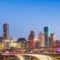 Vista noturna em Houston Texas, com arranha-céus iluminados e um viaduto sobre um rio, com rastros de luz de carros em movimento ao entardecer