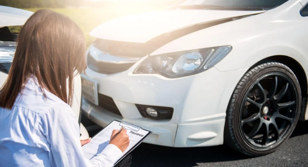 Persona junto a un auto blanco, revisando los documentos del seguro LDW y completando un formulario al aire libre, con detalles del neumático y el faro visibles.