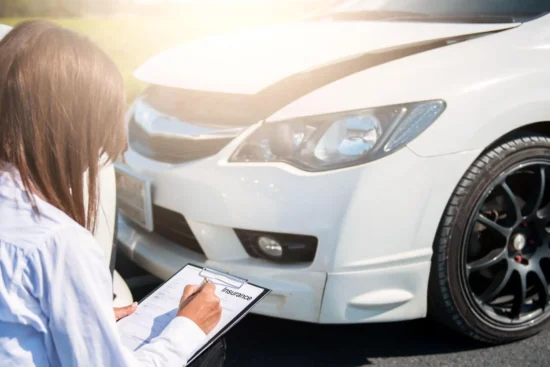 Persona junto a un auto blanco, revisando los documentos del seguro LDW y completando un formulario al aire libre, con detalles del neumático y el faro visibles.