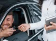 Atendimento em carro: motorista sorridente recebe as mãos de um consultor que entrega a chave do carro, sugerindo suporte ou verificação de informações durante a entrega.