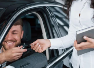 Atendimento em carro: motorista sorridente recebe as mãos de um consultor que entrega a chave do carro, sugerindo suporte ou verificação de informações durante a entrega.