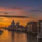 Pôr do sol em Veneza com o Grand Canal ao centro e a Basílica de Santa Maria della Salute ao fundo, cercada por edifícios históricos e águas refletindo o céu.