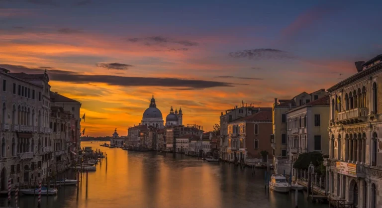 Pôr do sol em Veneza com o Grand Canal ao centro e a Basílica de Santa Maria della Salute ao fundo, cercada por edifícios históricos e águas refletindo o céu.